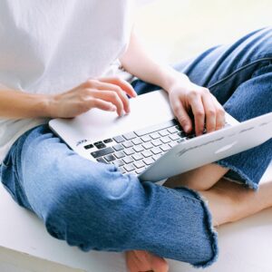 Woman sitting cross-legged in casual jeans working on a laptop indoors.