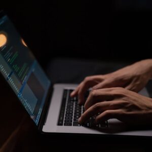 Hands typing code on a laptop keyboard in a dark room, capturing the essence of late-night programming.